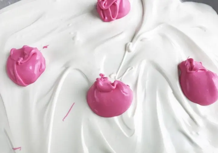 Melted bright pink candy dollops about to be swirled into a white candy base.