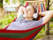 Young woman in headphones listening to music while resting in hammock outdoors