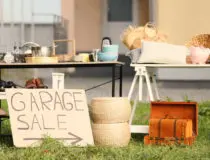 Sign Garage sale written on cardboard near tables with different