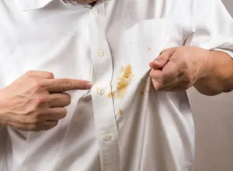 Person pointing to spilled curry stain on white shirt