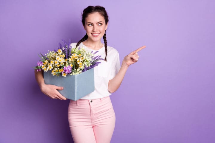 Portrait of pretty positive person hold wild flowers look direct finger empty space isolated on purple color background
