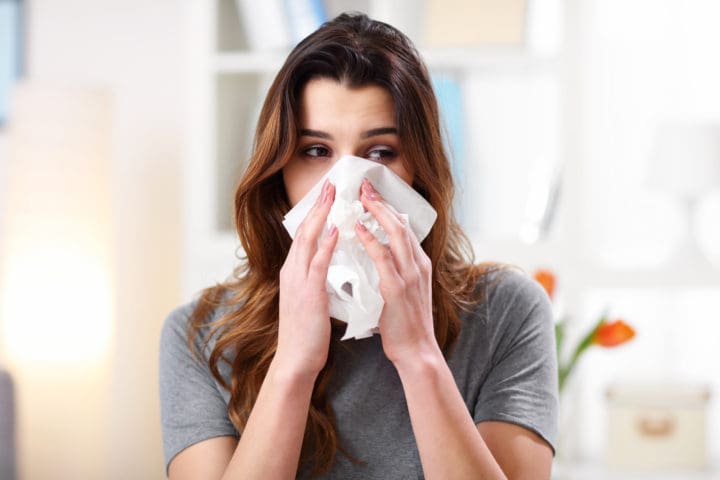 Hay fever treatment How to deal with sneezing season Pretty woman sneezing on tissue on couch in the living room