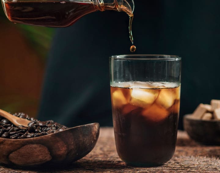 Pouring cold brew iced coffee in glass cup with ice cubes