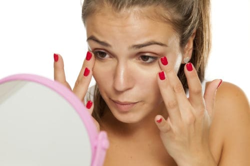 young women applied concealer under the eyes with her fingers