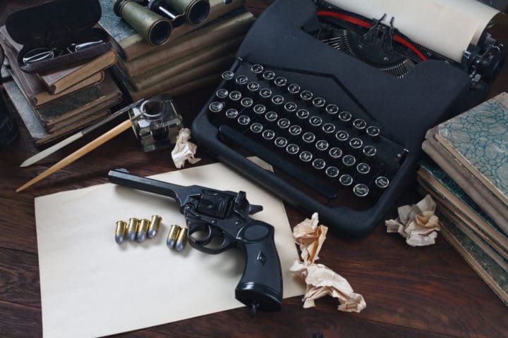 Writing a crime fiction book old retro vintage typewriter and revolver gun with ammunitions, books, papers, old ink pen