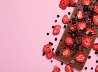 Chocolate bar with freeze dried fruits on pink background, flat