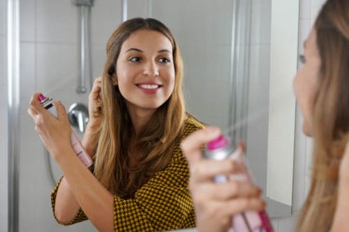 Beautiful young woman applying dry shampoo on her hair before go