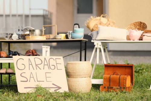 Sign Garage sale written on cardboard near tables with different