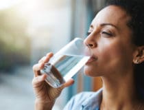 Drinking water, glass and woman thinking of healthcare, wellness and self care at home Fresh, clean liquid and african person in window of her house with vision for health, diet and nutrition