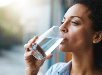 Drinking water, glass and woman thinking of healthcare, wellness and self care at home Fresh, clean liquid and african person in window of her house with vision for health, diet and nutrition