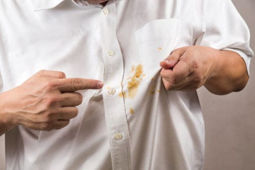 Person pointing to spilled curry stain on white shirt