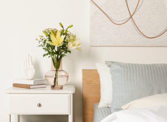 Vase with bouquet of fresh flowers on white nightstand in bedroom
