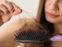 Woman untangling her hair from brush on light background, closeup