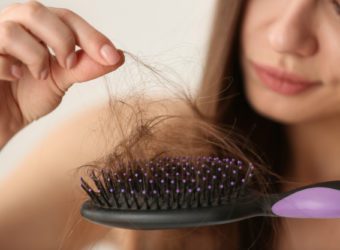 Woman untangling her hair from brush on light background, closeup