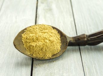 Spoon with Kava Kava root powder on wooden table closeup