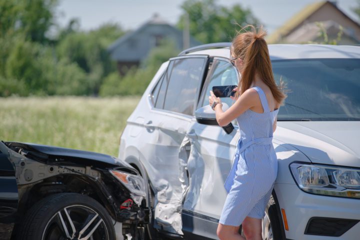 Stressed driver taking picture on sellphone camera of smashed vehicle calling for emergency service help after car accident Road safety and insurance concept