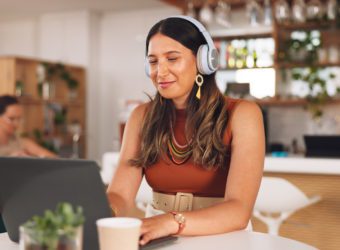 Laptop, freelance and woman in coffee shop with headphones, online research career and smile Communication, technology and remote work, happy girl in cafe at computer, virtual assistant and internet