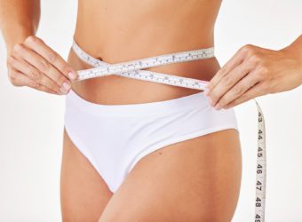 Trying to reach my weight goals a model measuring herself using tape measure against a studio background